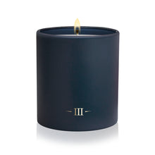 Load image into Gallery viewer, A dark navy blue matte candle in a matching cylindrical container, lit with a visible flame and featuring a gold Roman numeral III logo on the front, set against a clean white background.