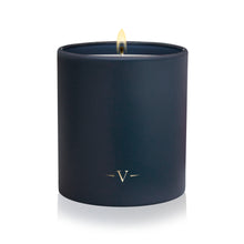 Load image into Gallery viewer, A navy blue matte candle in a matching cylindrical jar, lit with a single flame and featuring a small gold monogram logo near the bottom, set against a clean white background.
